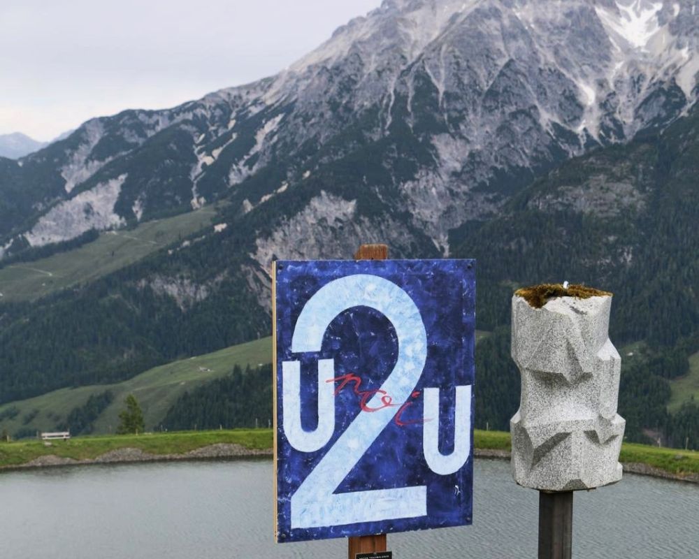 Das Kunstwerk ist Teil der Ausstellung „Weltbilder“ am Kunstwanderweg in Leogang. Die Ausstellung wurde von Anton Thuswaldner gemacht. Zu sehen ist eine Tafel mit einem Bild auf blauem Hintergrund. In der Mitte steht eine große Zahl 2, daneben die Buchstaben U2U. In roter Schrift steht das Wort moi. Daneben steht eine graue Steinskulptur. Im Hintergrund sieht man einen See und hohe Berge.
